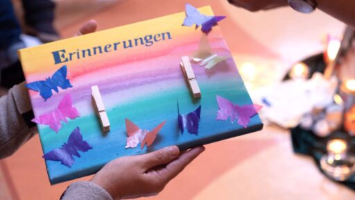 Ein Bild mit einem gemalten Sonnenuntergang, dem Wort Erinnerung und aufgeklebten Schmetterlingen aus Papier
