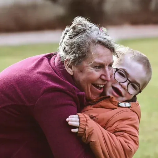 Eine Löwenherz-Pflegekraft umarmt einen kleinen Jungen, beide lachen.